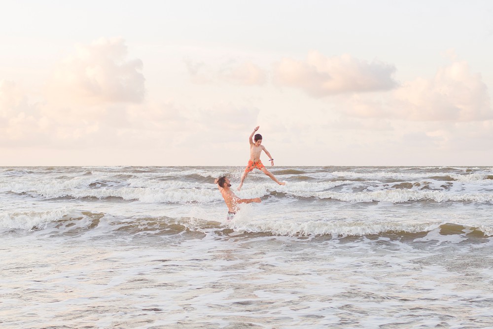 Father tossing his son into the waves at their Galveston beach family session