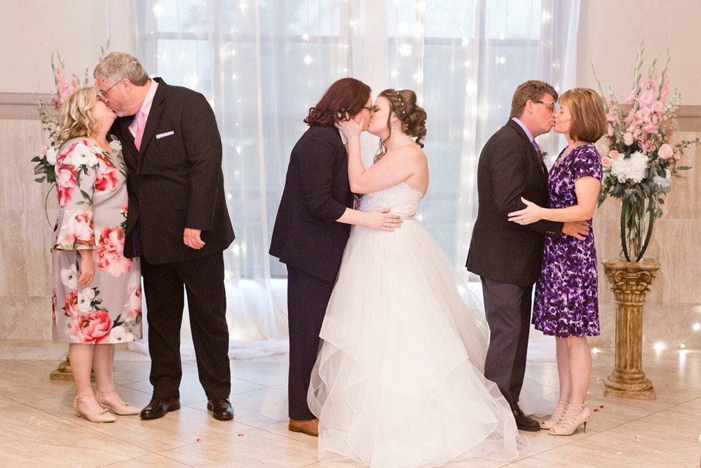Bride and bride kissing with bride's parents kissing