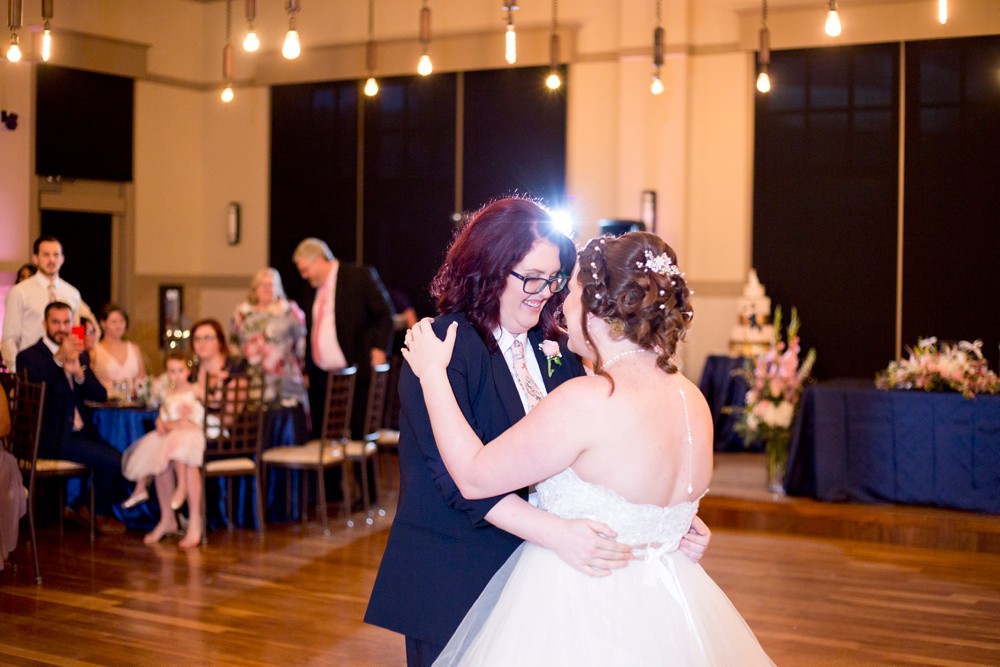 Bride and bride share their first dance under the Edison bulb lighting at Noah's Event Venue