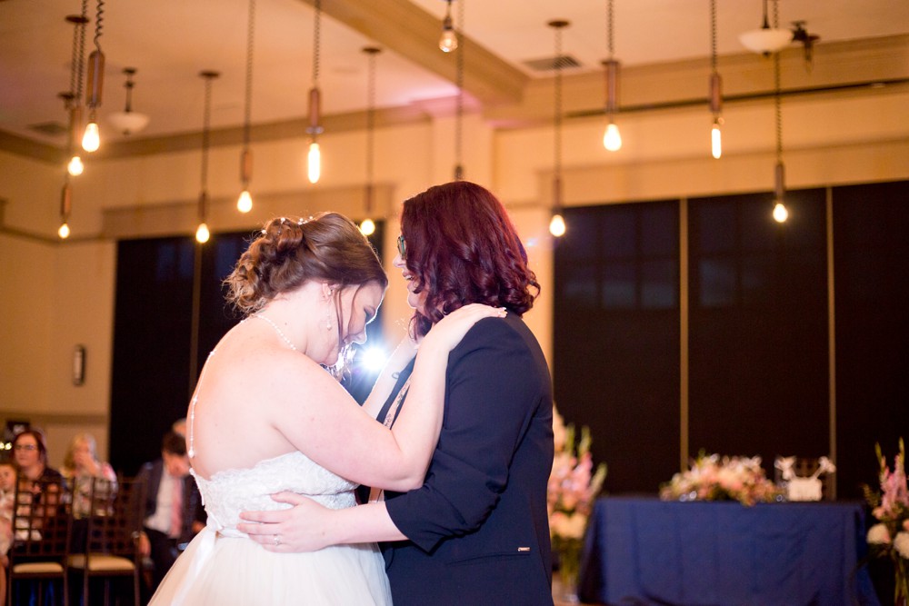 Bride and bride share their first dance under the Edison bulb lighting at Noah's Event Venue