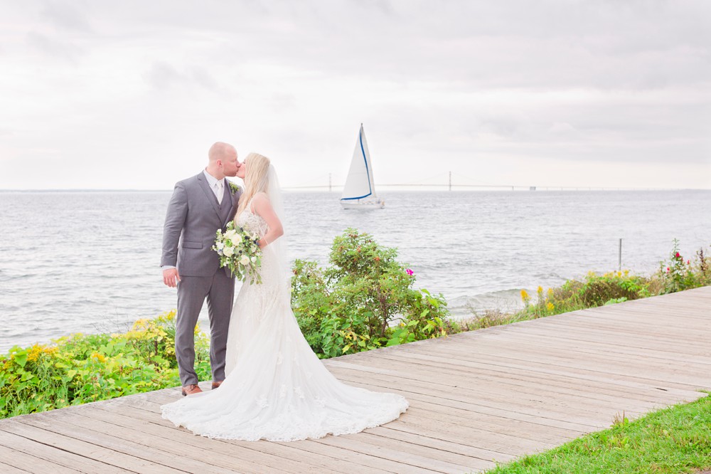 Bride and groom kissing with a sailboat and the Mackinac Bridge in the background