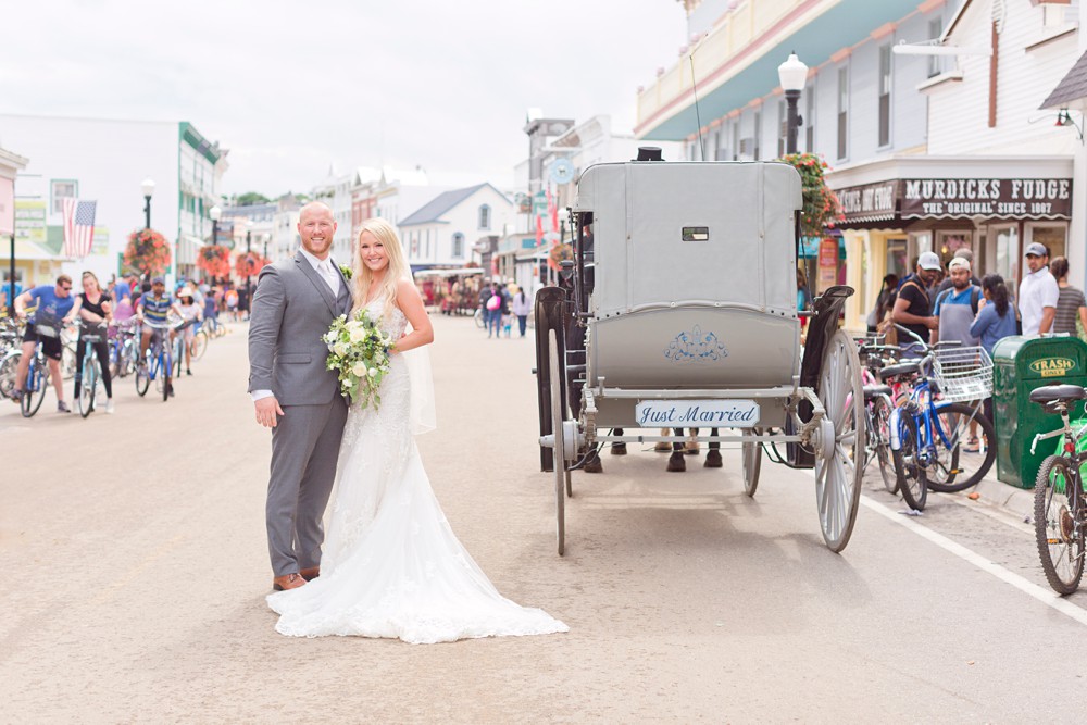 Bride and groom portrait next to horse drawn carriage in the middle of Main Street on Mackinac Island