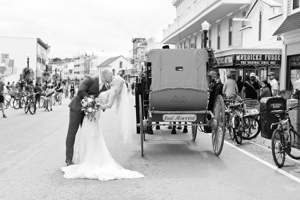 Bride and groom kissing next to horse drawn carriage in the middle of Main Street on Mackinac Island