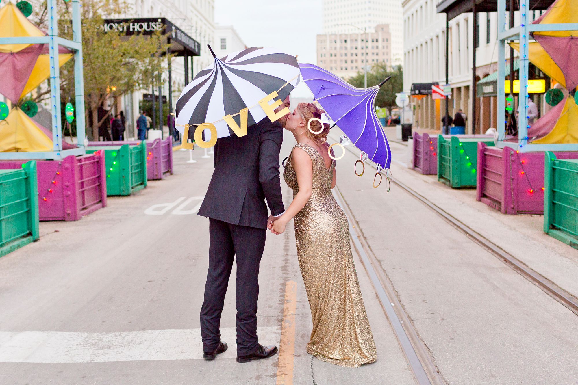 A bride and groom with Mardi Gras umbrellas kiss under the Powell Mardi Gras Arch in Galveston, Texas.