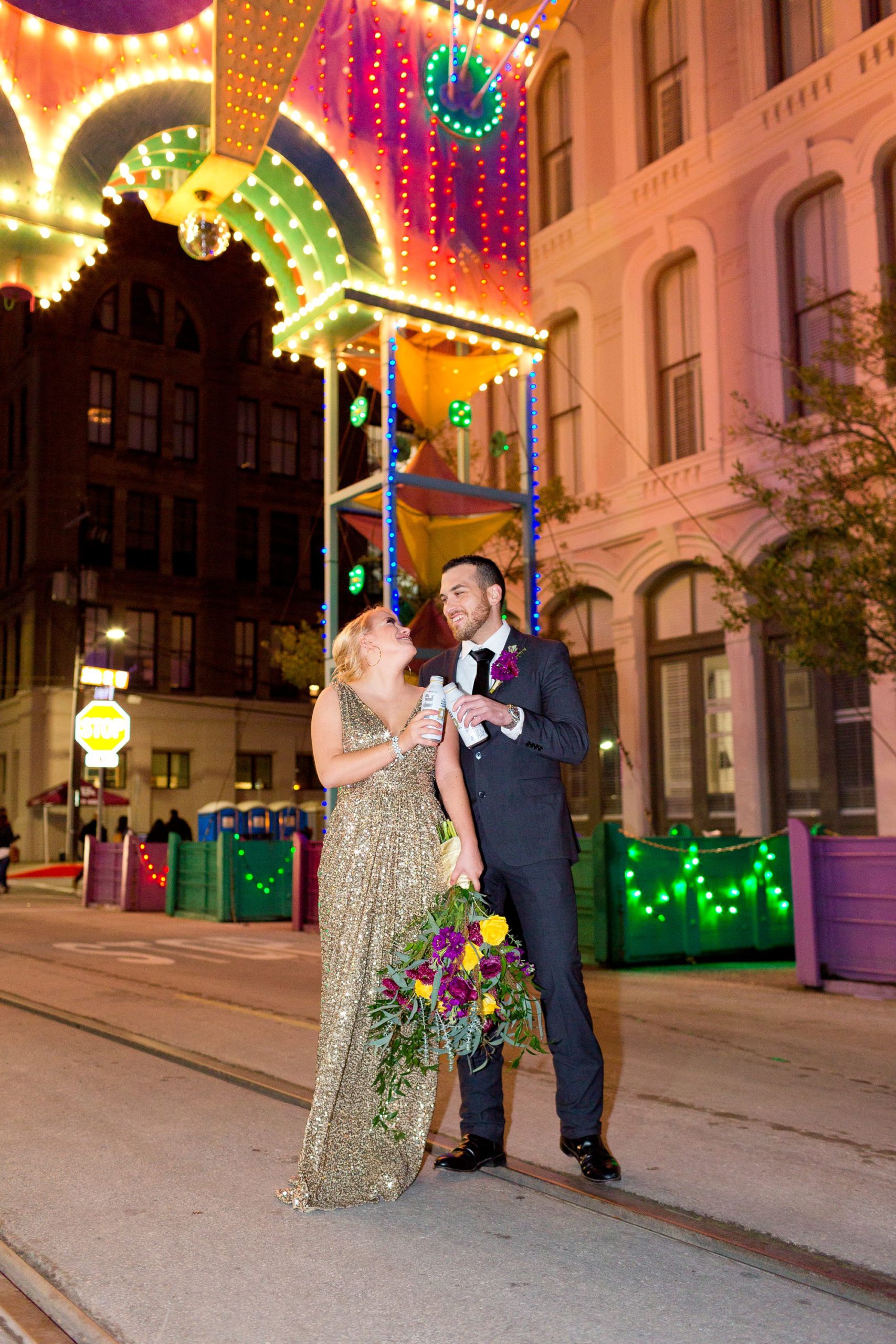 A bride and groom toast with beers under the Powell Mardi Gras Arch in Galveston, Texas.