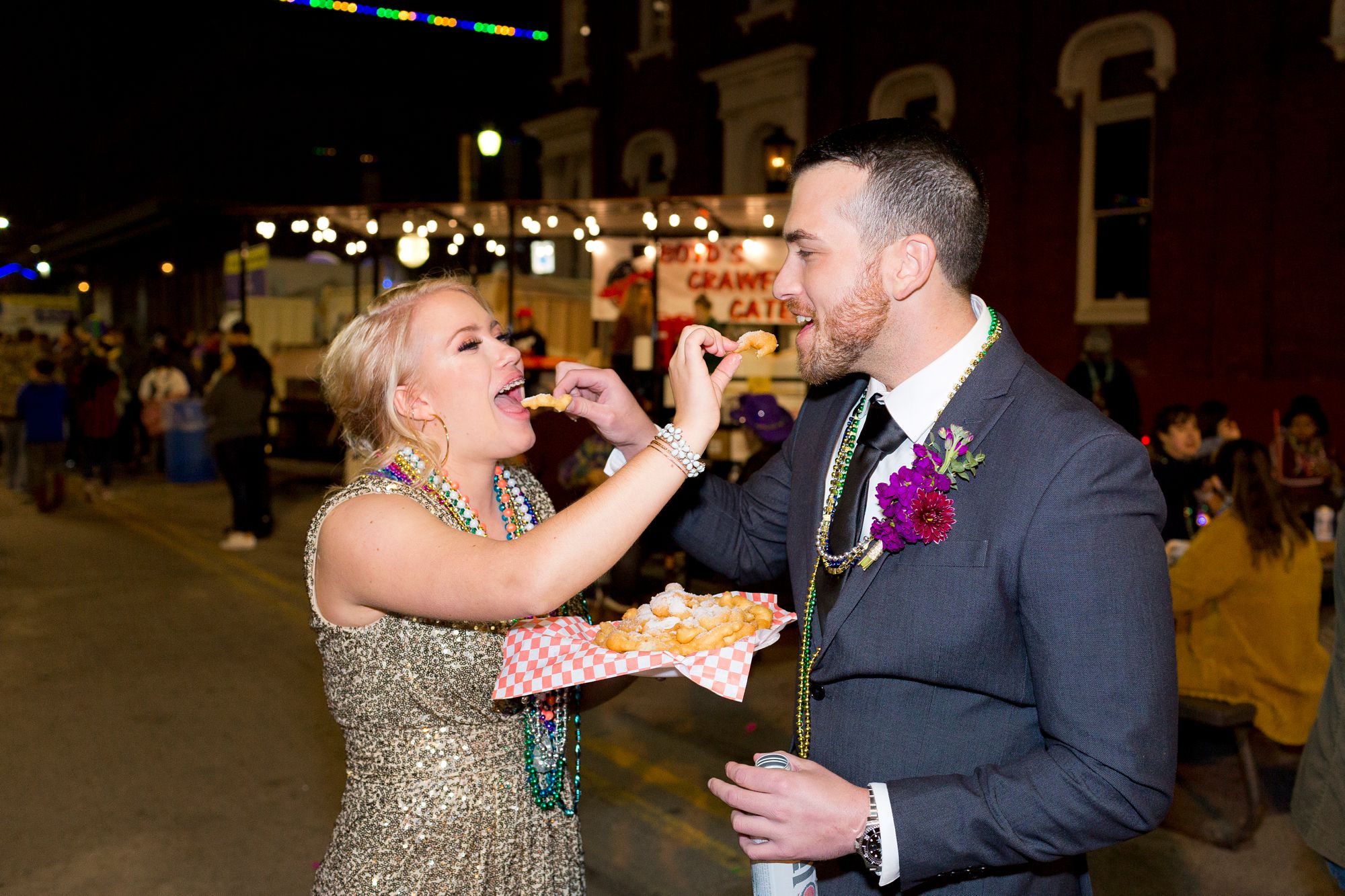 A bride and groom feed each other funnel cake at their Mardi Gras Galveston elopement.