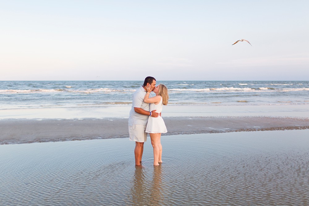 Couple taking engagement photos on Galveston Island beach at sunset