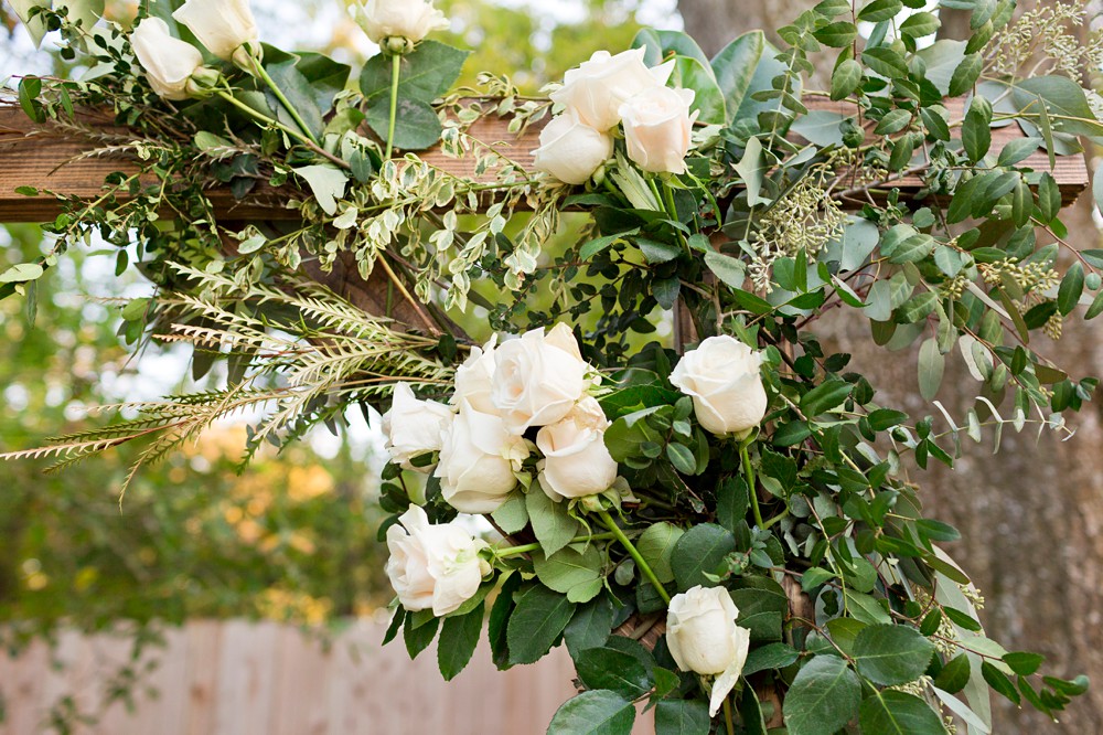 White roses and greenery decorating a wedding ceremony arch