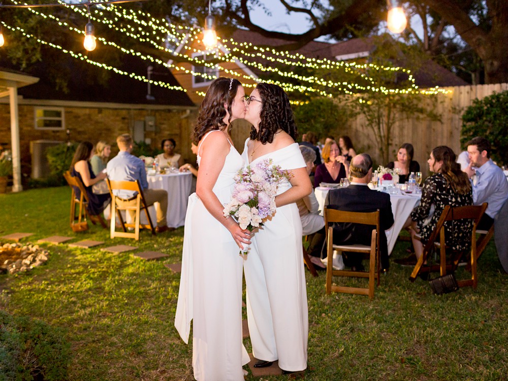 Brides kissing under string lights at their intimate backyard Houston wedding
