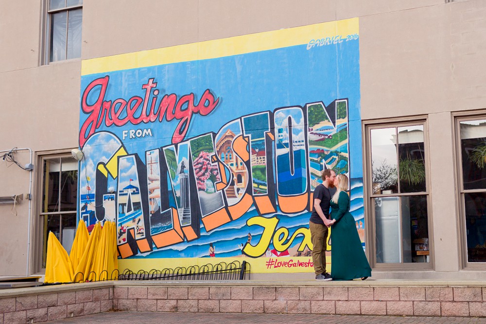 Couple posing in front of the Greetings from Galveston mural at Saengerfest Park