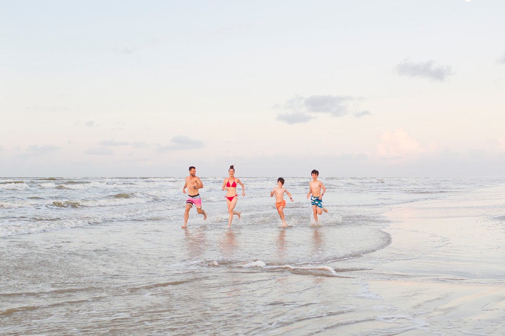 family running in the ocean at their sunrise Galveston beach family session