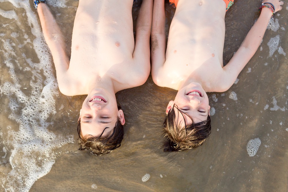 two brothers laying in sand at the beach