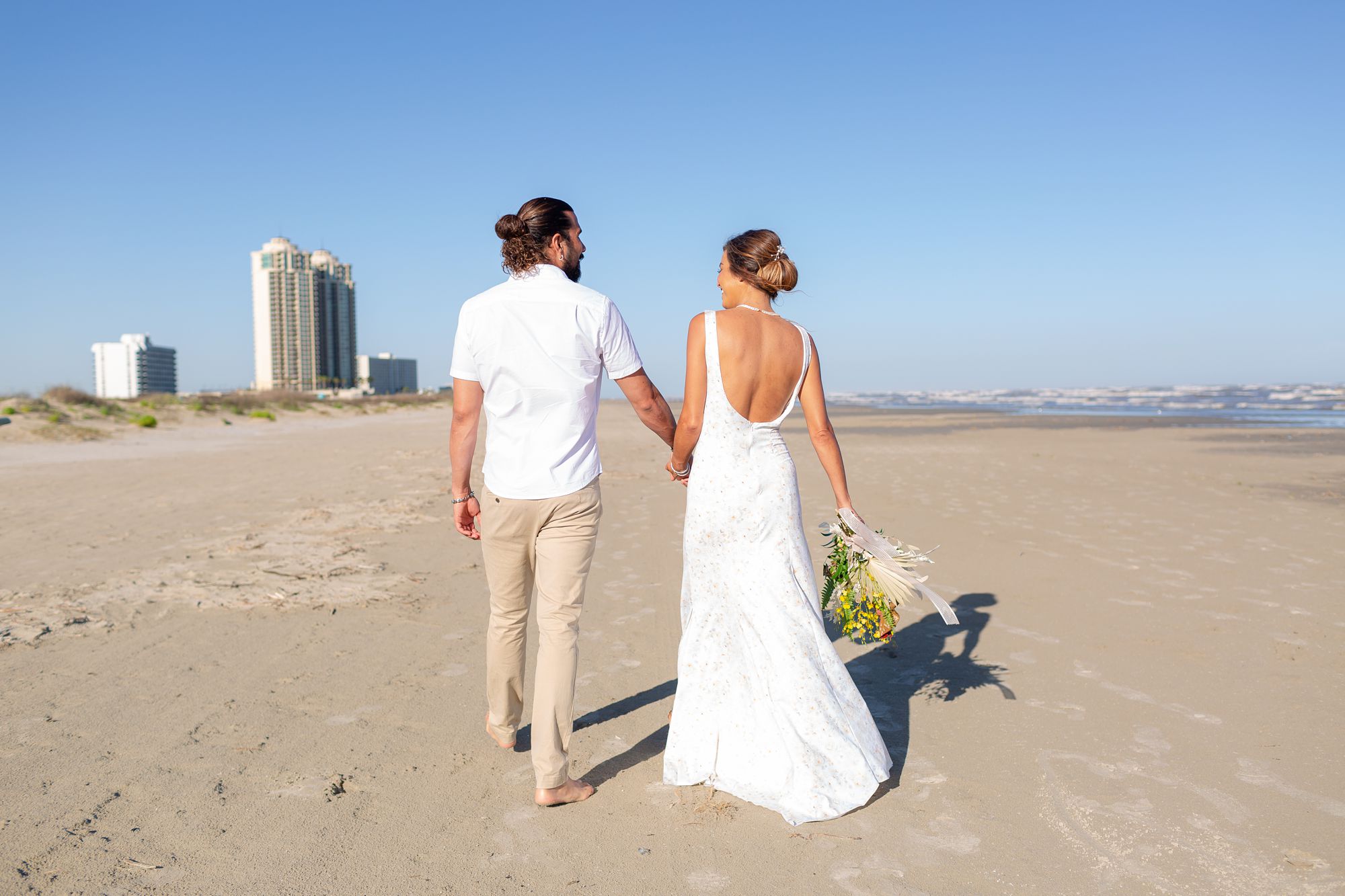 A bride and groom walk along a beach in Galveston, Texas.