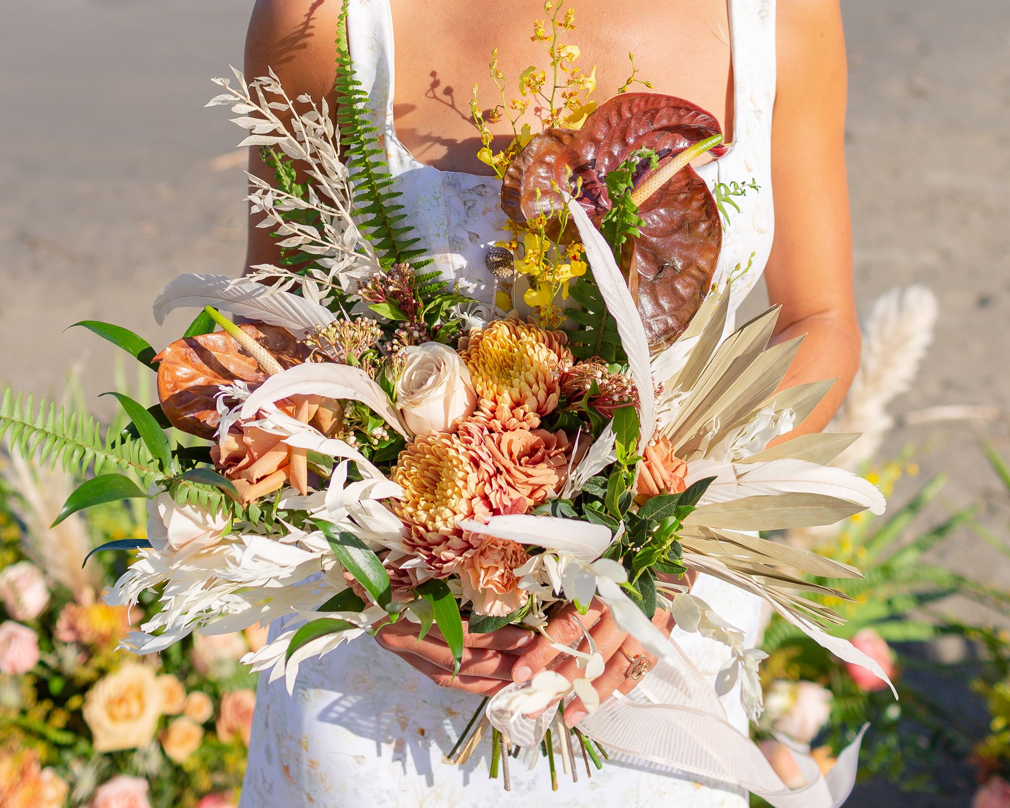 A pink, orange and yellow tropical boho wedding bouquet with orange roses and feathers.