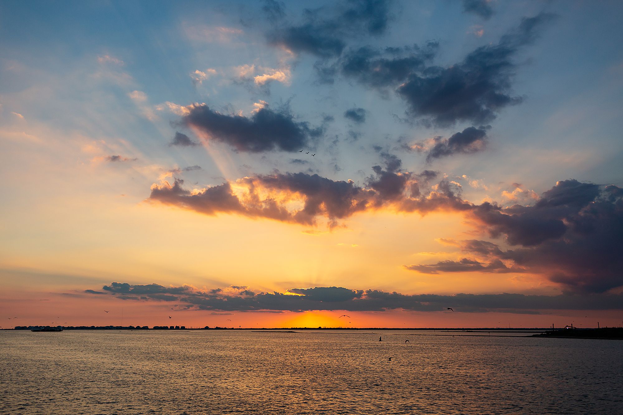 The sun sets behind a cloud in Galveston's West Bay.