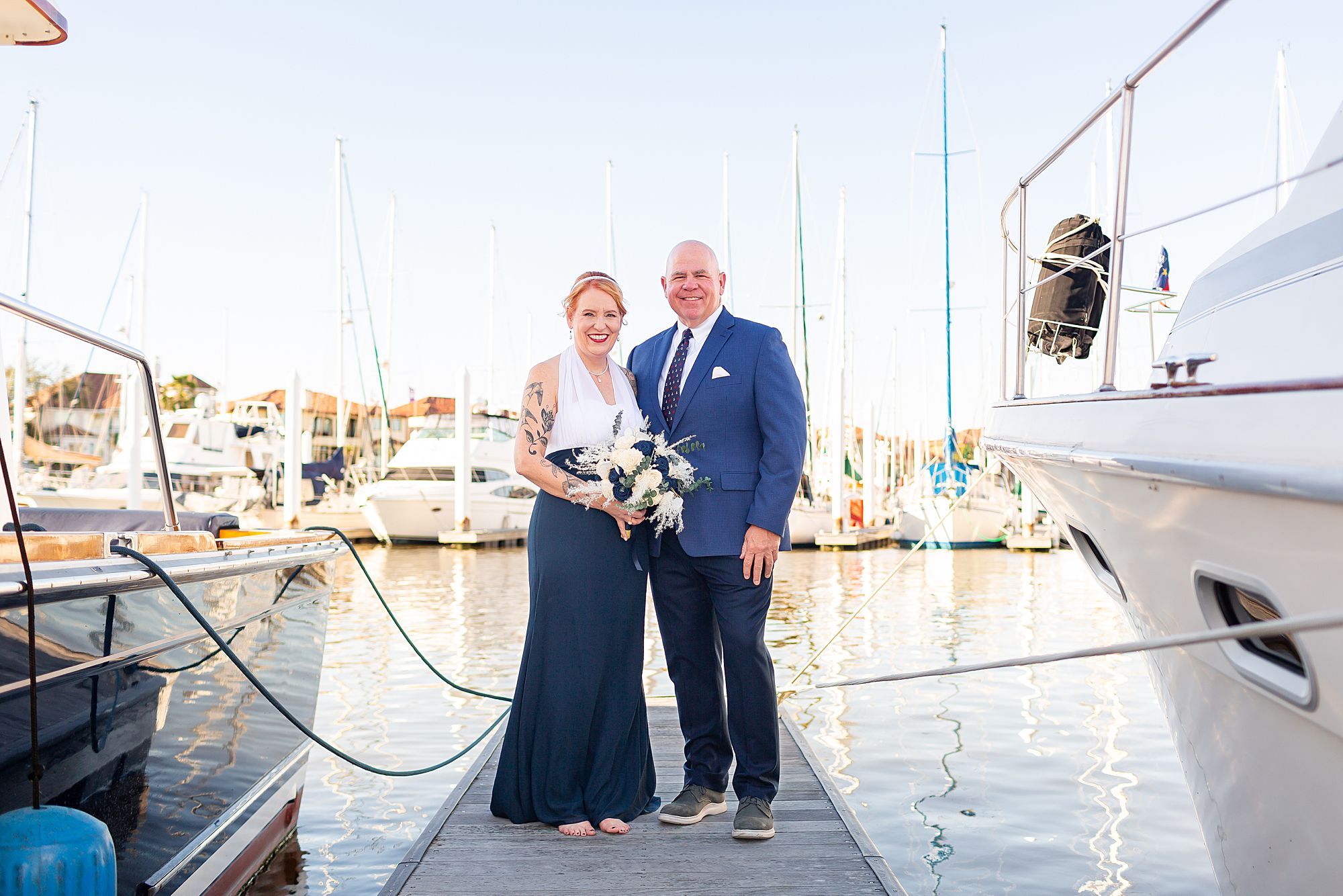 A bride in a navy blue and white dress stands with a groom in a blue suit on a dock in Kemah, Texas.