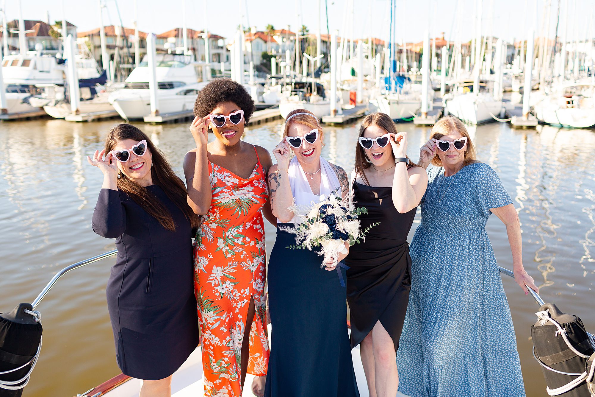 Elopement guests and a bride wearing heart shaped sunglasses pose on the bow of a yacht in Kemah, Texas.