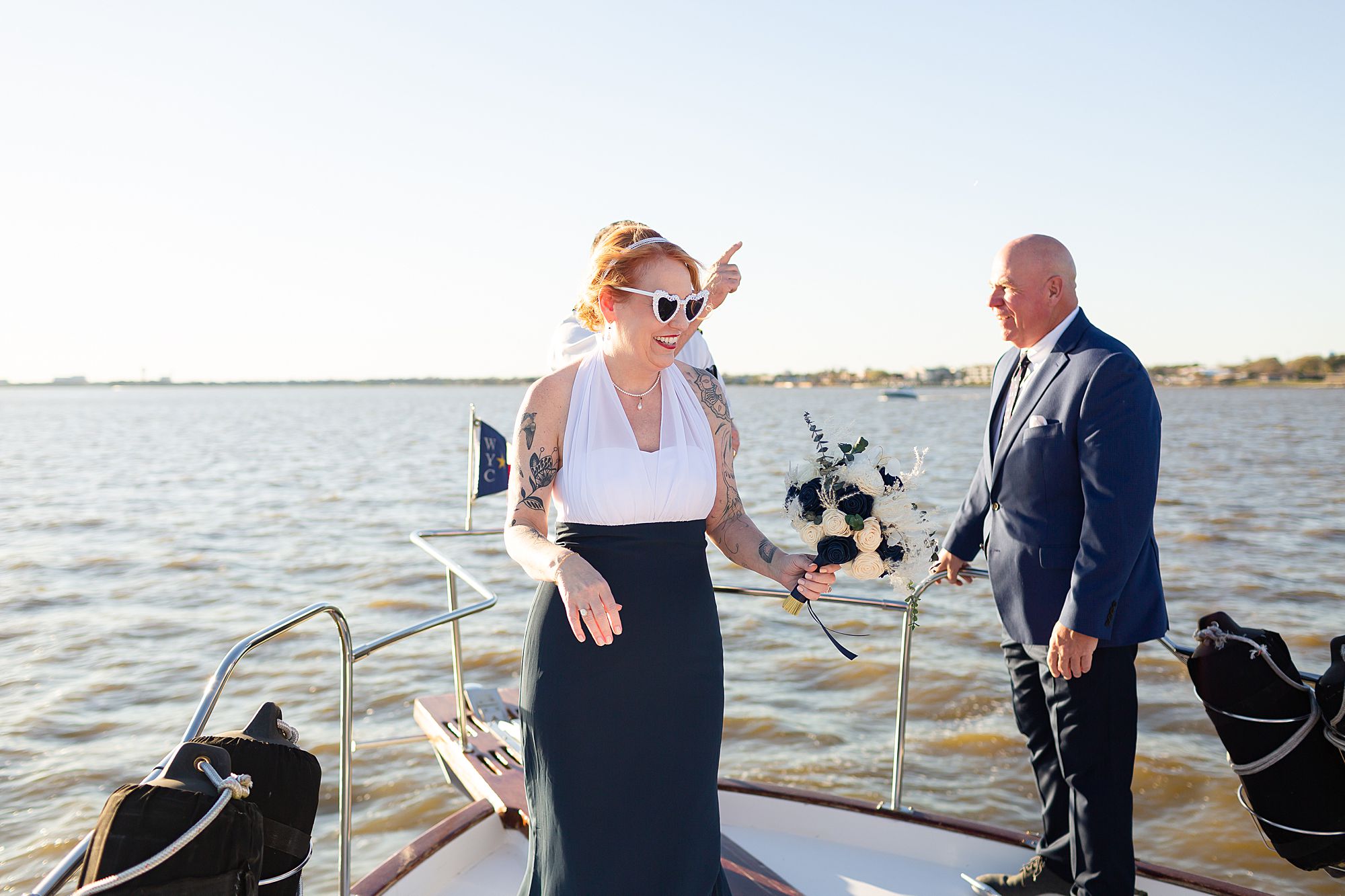 A bride in heart shaped sunglasses laughs as she meets her groom on the bow of a yacht on Clear Lake in Kemah, Texas.