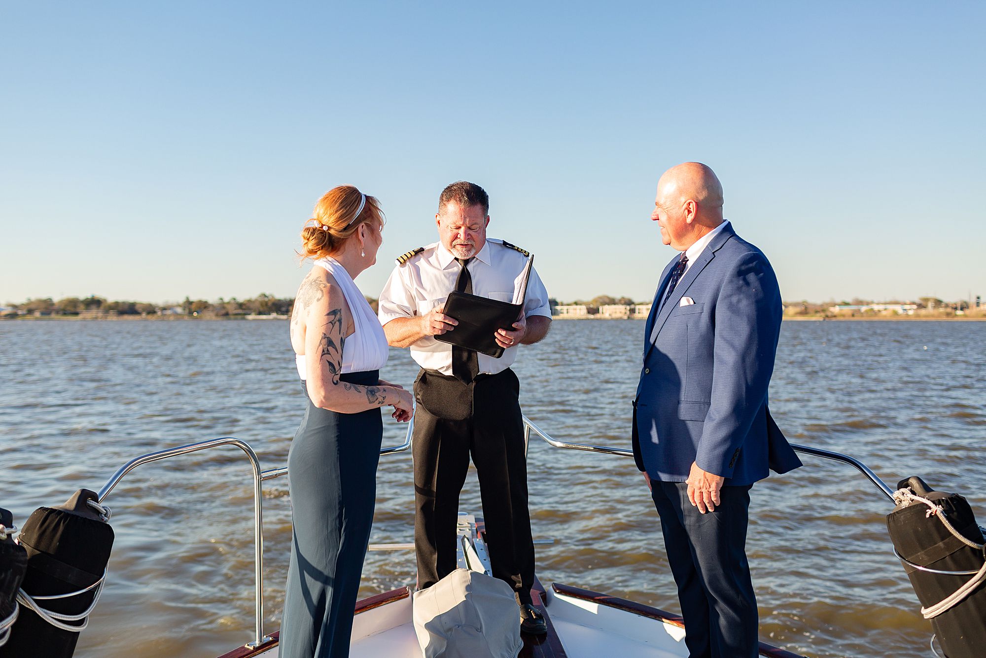 A bride and groom stand on the bow of a yacht while the captain conducts their elopement ceremony.