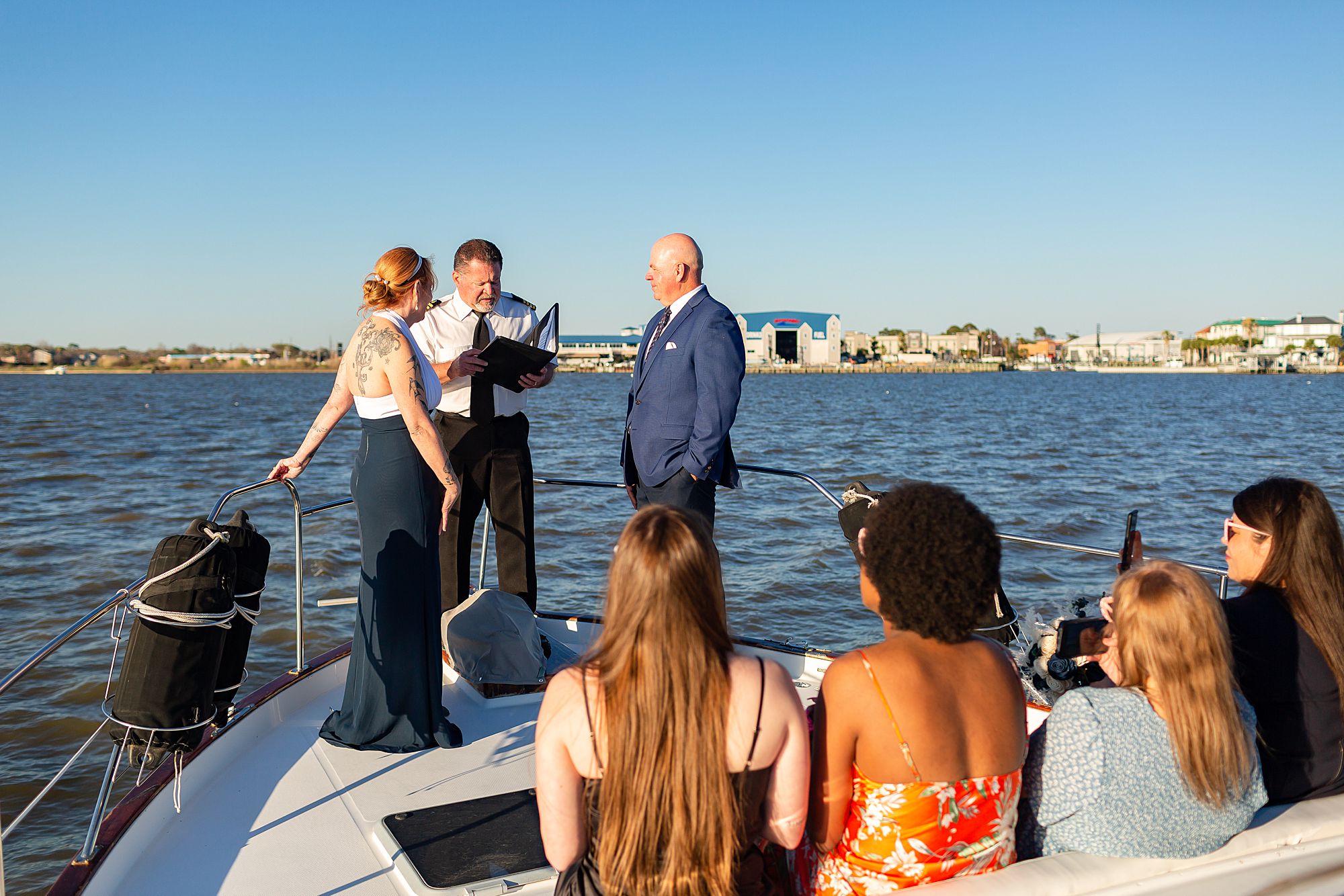 Elopement guests look on as a bride and groom share vows on the bow of a yacht in Kemah, Texas.