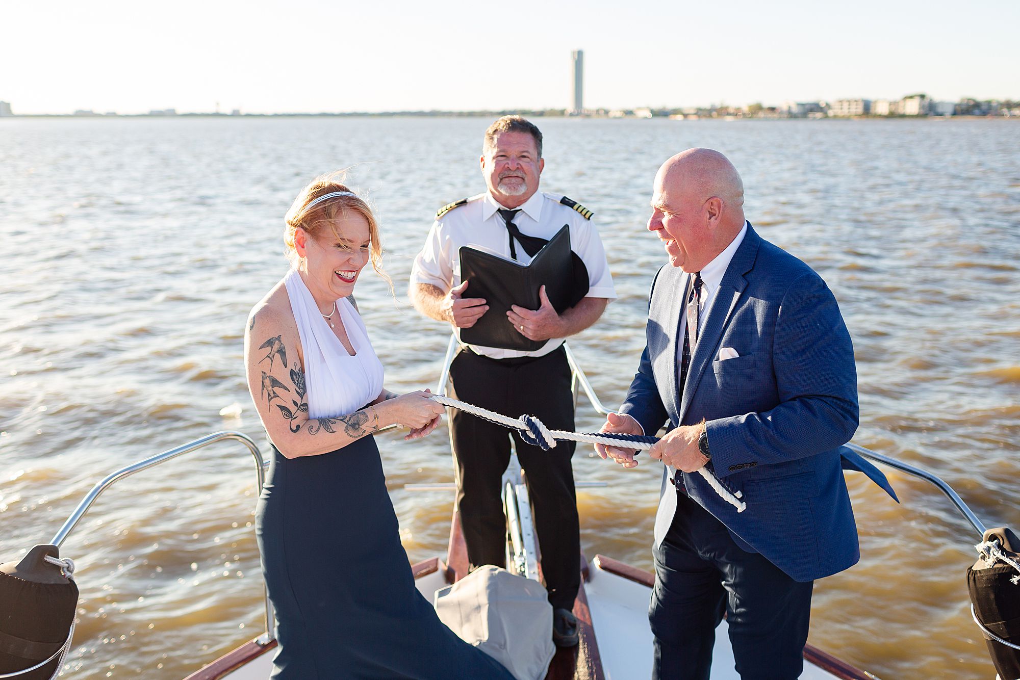 A bride and groom laugh as they tie a knot with a white and blue rope at their Kemah yacht elopement.