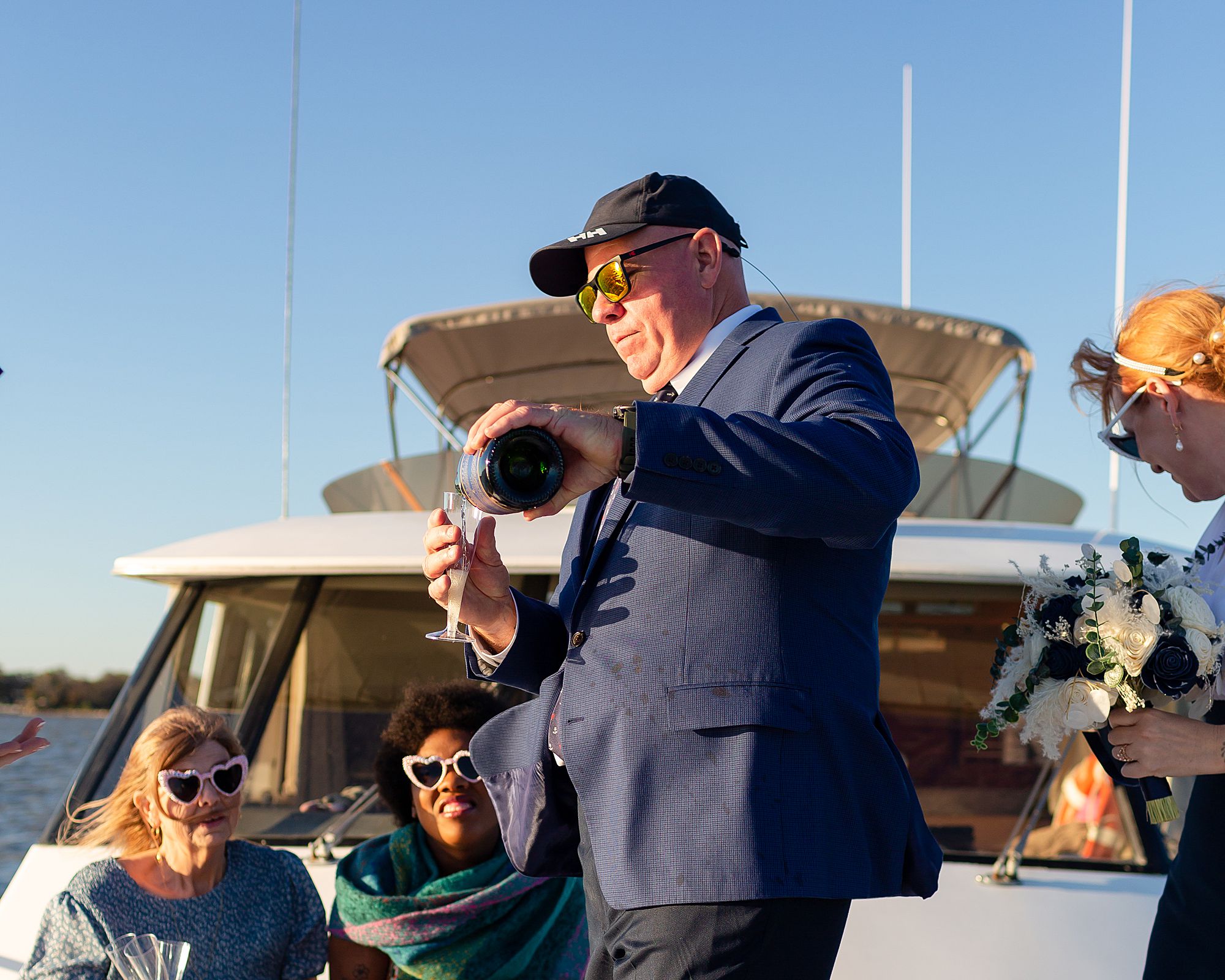 A groom pours champagne for guests on a yacht during sunset.