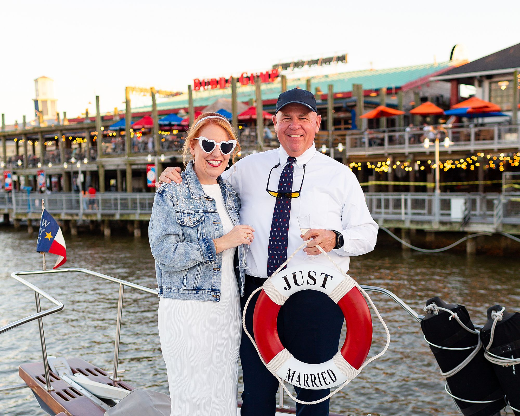 A bride and groom pose with a red and white life ring that says just married with Kemah Boardwalk in the background.