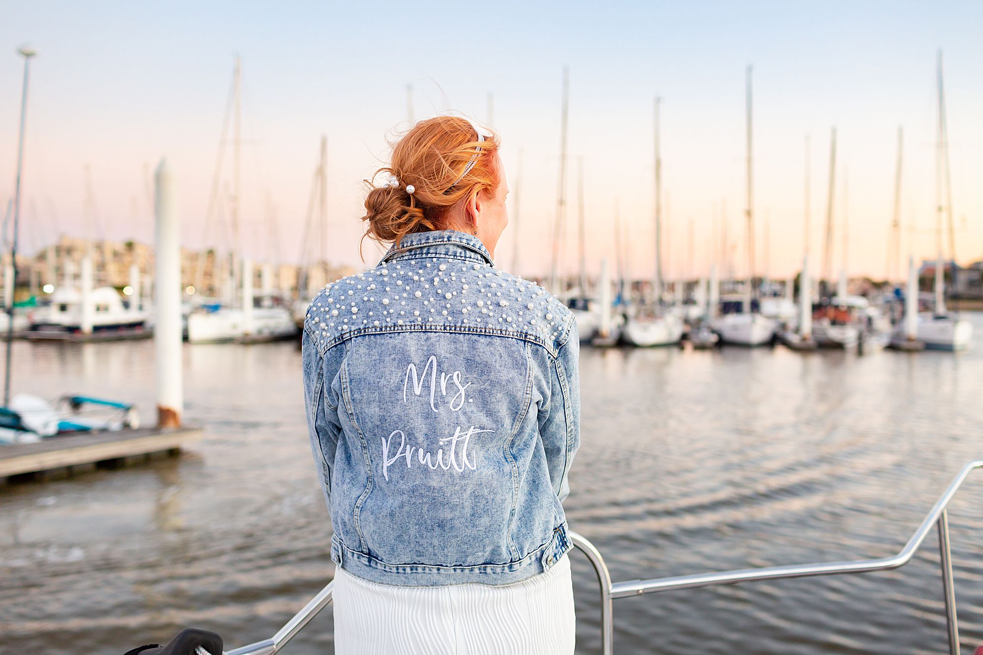 A bride wears a denim jacket with her new last name embroidered on the back and pearl detailing.