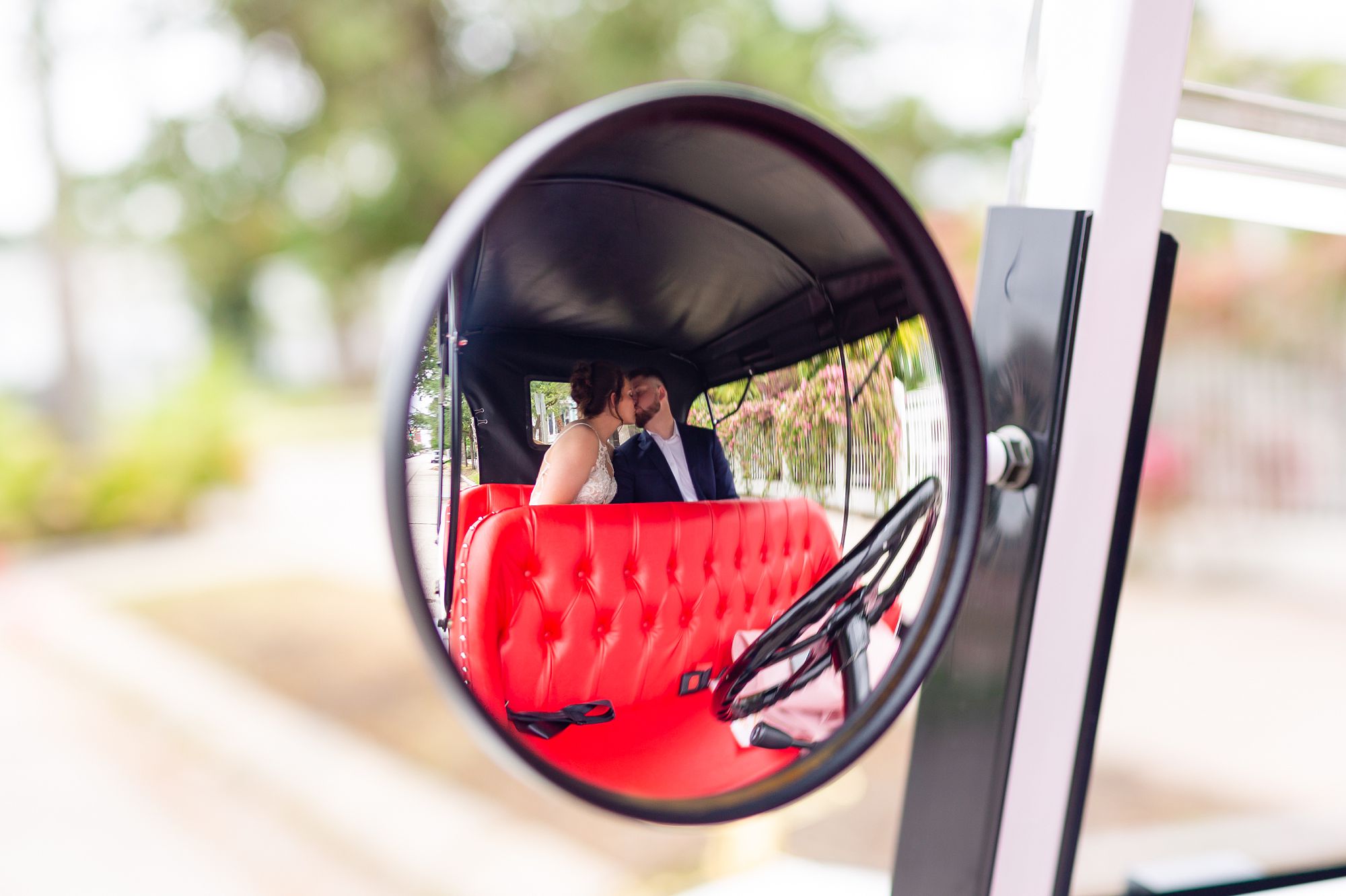 A bride and groom kiss in the backseat of a Model T style golf cart at their elopement style anniversary on Galveston Island.
