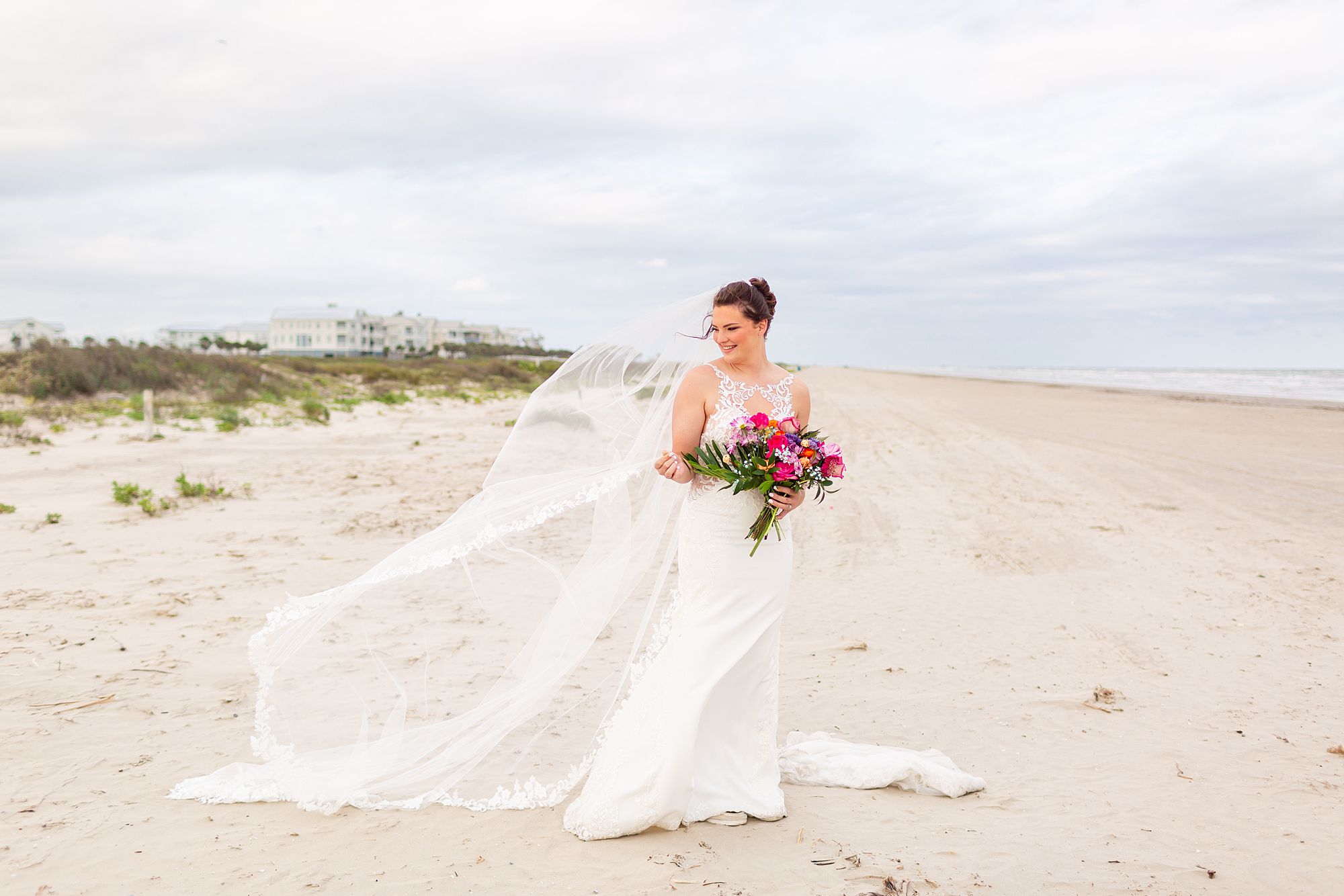 A bride holds the edge of her veil as the wind gently blows it behind her.