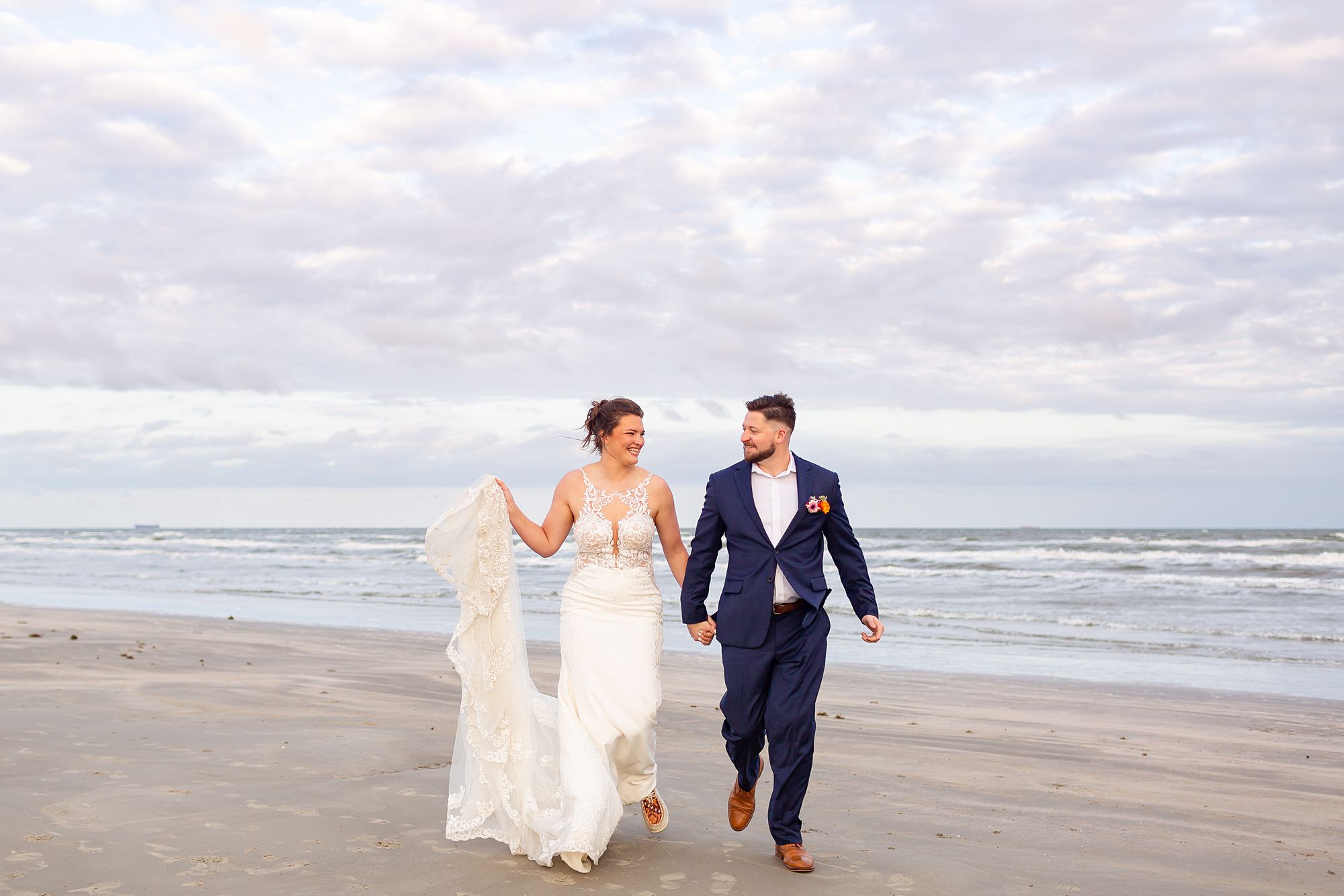 A bride and groom walk on a Galveston beach at sunset.