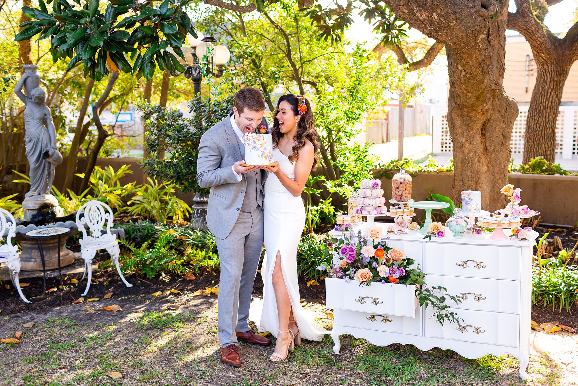 A groom pretends to take a large bite out of a purple wedding cake that him and his bride are holding.